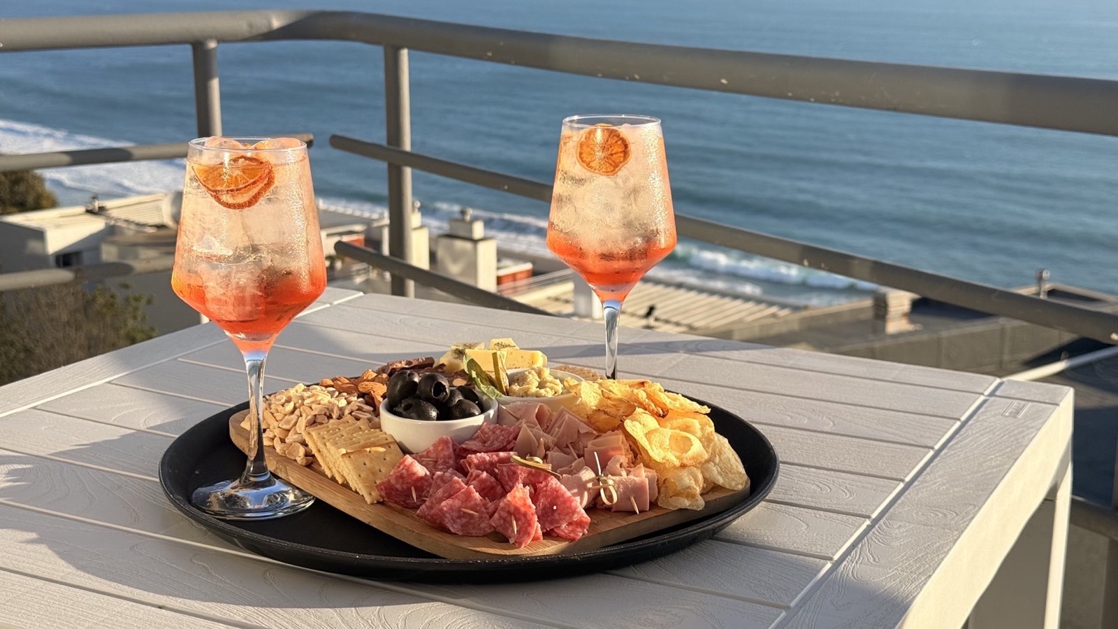 Tabla y cócteles del Dei Bar servidos en el balcón frente al mar